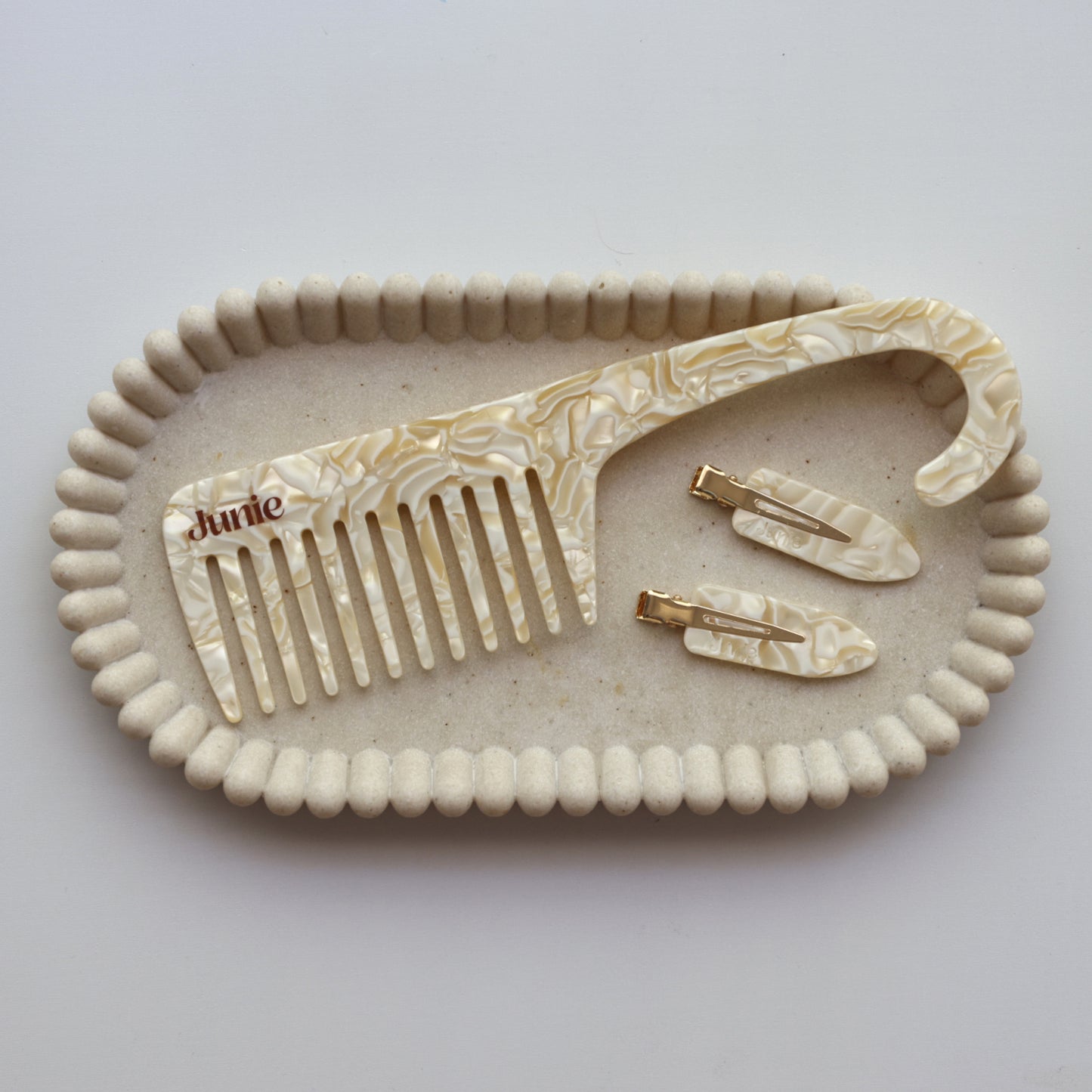 Junie wide-tooth comb and set of hair clips on a decorative tray with 'Junie' branding. Featuring soft natural light, perfect for hair care routine.
