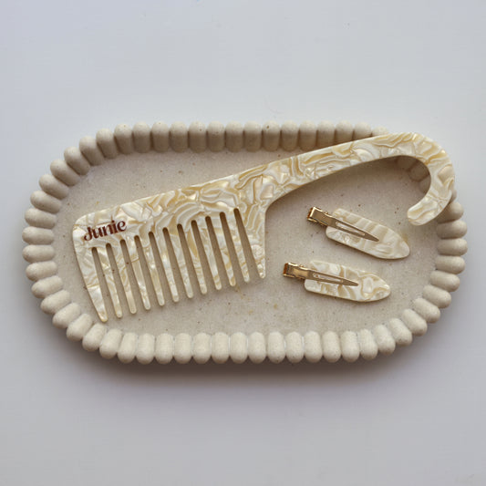Junie wide-tooth comb and set of hair clips on a decorative tray with 'Junie' branding. Featuring soft natural light, perfect for hair care routine.