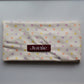 A folded fairy bread cream-colored hair drying towel with a pastel polka dot pattern in pink, purple, yellow, and orange, featuring a dark red rectangular label with the name 'Junie' in white text.