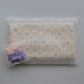 A folded cream-coloured Junie quick dry hair towel kids item with pastel multicolor polka dots, sealed inside a clear plastic zip pouch. A small clear plastic bag containing two silk scrunchies, one pink and one purple, sits in the lower-left corner.