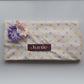 A fabric quick dry hair towel with a cream background and pastel polka dots in pink, purple, and yellow, featuring a maroon label that reads 'Junie' and two silk scrunchies on top.