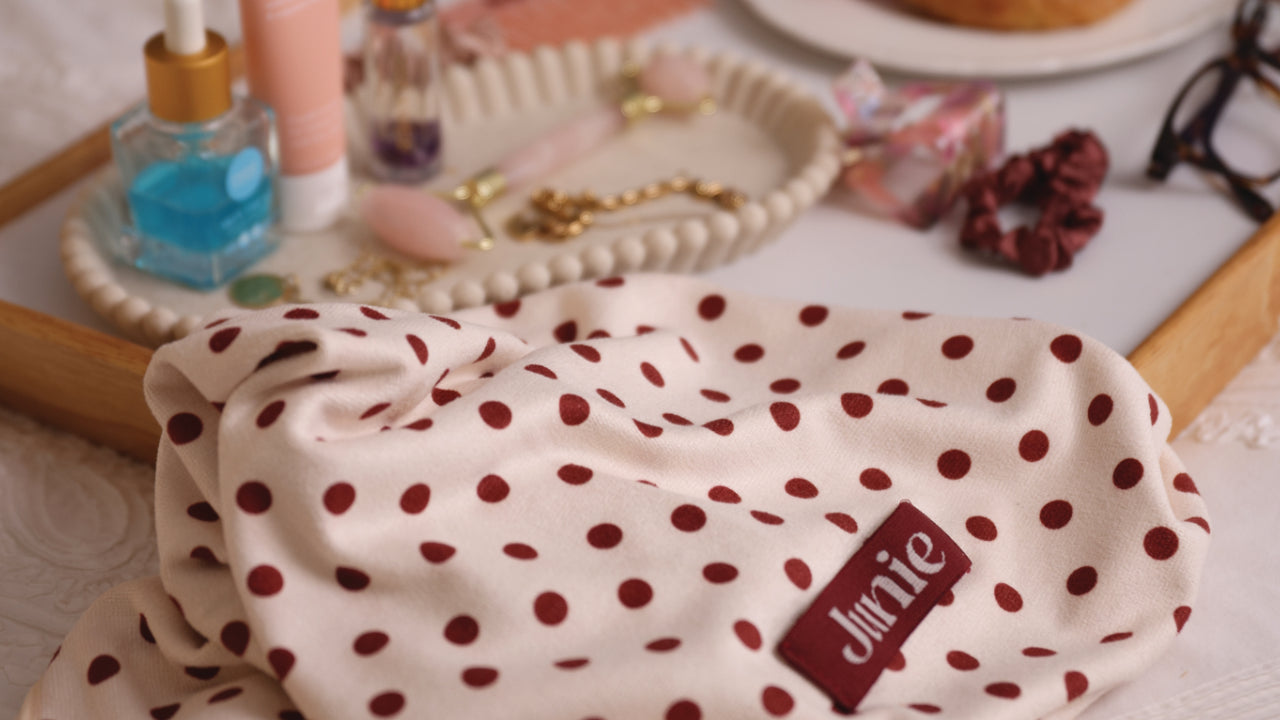 Polka dot fabric with the brand label Junie on a table with various self-care items in the background.
Junie fast-drying signature blend microfibre hair towel wrapped on wet hair, designed to absorb moisture quickly while reducing frizz, breakage and heat damage. Helps reduce heat styling and blow-drying time.
